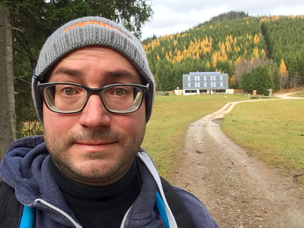 Das Gesicht eines verschwitzten Wanderinformatikers neben der
      Ansicht des Naturfreundehauses Knofeleben